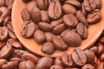 Roasted coffee beans on a saucer, against a background of many coffee beans
