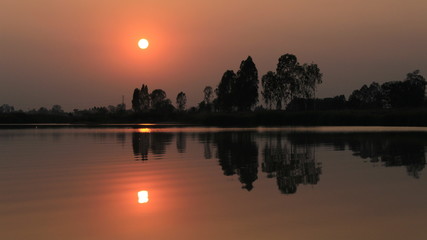  silhouette tree in asia with sunset.Tree silhouetted against a setting sun.Dark tree on open field dramatic sunrise and reflection in water.
