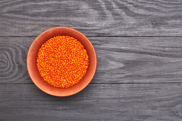 lentil grains in a plate on a black wooden background.