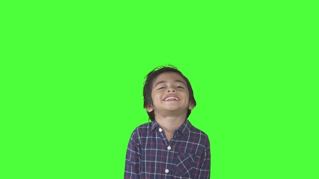 Cute little boy smiling at the camera while standing in the studio. Shot in 4k resolution with green screen background