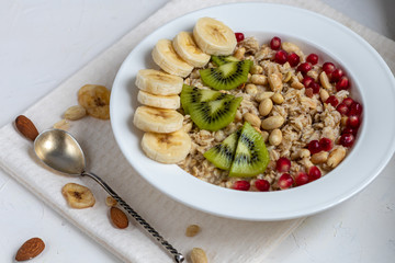 Breakfast consisting of oatmeal, nuts and fruits. Kiwi, banana, pomegranate and almonds decorate the plate. Healthy food, on a white background.
