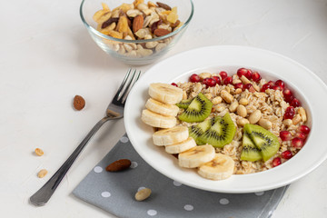 Breakfast consisting of oatmeal, nuts and fruits. Kiwi, banana, pomegranate and almonds decorate the plate. Healthy food, on a white background.