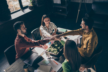 Above high angle view of four nice cheerful experienced professional businesspeople wearing casual formal-wear shaking hands deal at modern industrial loft brick style interior work place station