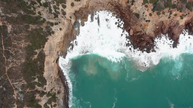 AERIAL: Serie of big waves break into the rocky beach in the algarve