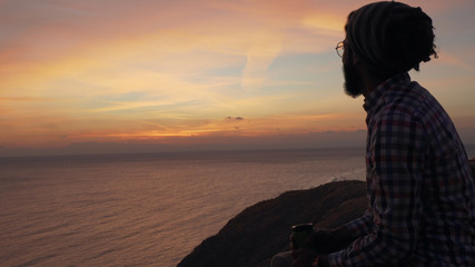 Fototapeta premium Handsome middle eastern male sitting on a cliff at sunrise
