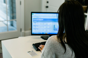 Rear view of brunette woman working on a computer in a small mostly white modern home office 