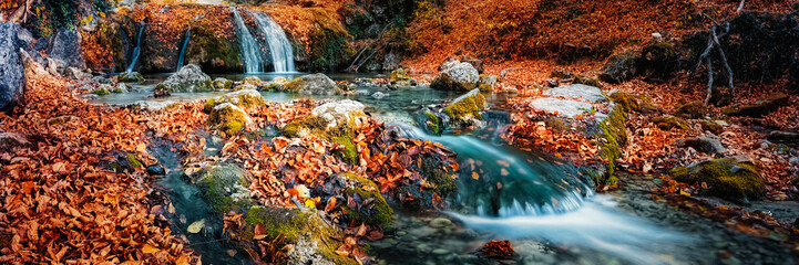 Waterfall cascade in the forest in autumn among the fallen colorful bright leaves.