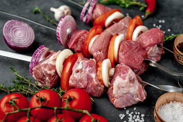 Raw skewers of meat. Barbecue meat with vegetables and spices on a stone background. 