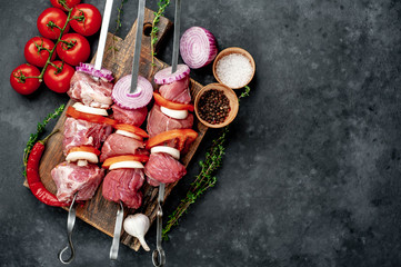 Raw skewers of meat. Barbecue meat with vegetables and spices on a stone background. 