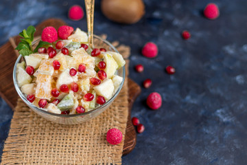 Diet fruit salad for breakfast. Kiwi orange banana and apple diced and seasoned with yogurt with honey. Healthy food, vegetarianism. On a dark background.