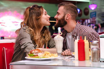 Loving couple sit in retro bright cafe eat french fries indoors.