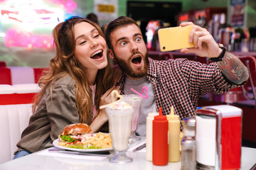 Young loving couple sit in retro bright cafe take a selfie