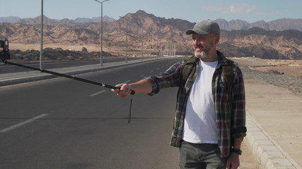 Hand-held shot of senior traveler male shooting himself with monopod