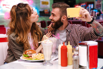 Young loving couple sit in retro bright cafe take a selfie