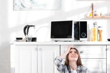 sad and attractive woman looking at broken microwave in kitchen