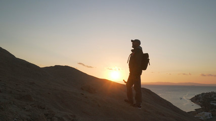 Fototapeta na wymiar Handsome senior traveler with selfie stick climb up a hill at sunrise