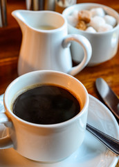 White cup with black coffee and  hot milk jug