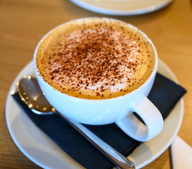 White cup with cappuccino coffee with cinnamon or cacao powder