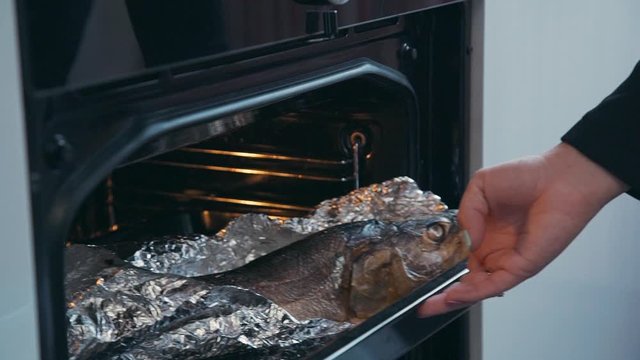 chef hands take out baking pan with cooked salmon fish from the heated oven. woman cook trout in foil. housewife homemade cooking on kichen. baking sheet on grill