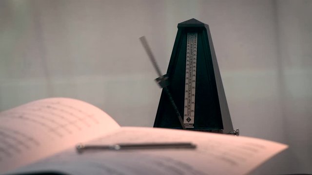 Metronom schl&auml;gt den Takt. Im Vordergrund liegen Noten und eine Stimmgabel, unscharf