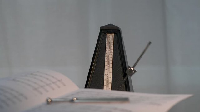 Metronom schl&auml;gt den Takt. Im Vordergrund liegen Noten und eine Stimmgabel, unscharf