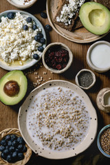 Healthy breakfast. Variety of breakfast dishes sprouted wheat, yogurt, kefir, cottage cheese, avocado, rye bread, seeds, nuts and berries assortment in ceramic bowls over wooden background. Flat lay