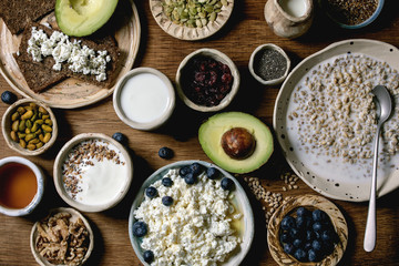 Healthy breakfast. Variety of breakfast dishes sprouted wheat, yogurt, kefir, cottage cheese, avocado, rye bread, seeds, nuts and berries assortment in ceramic bowls over wooden background. Flat lay