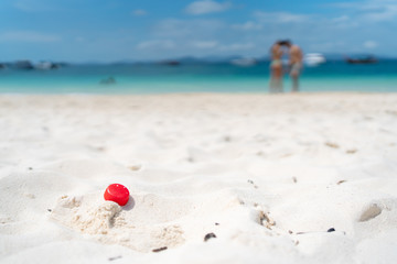 Red Plastic bottle caps on the sand with blurred tourist lovers background,