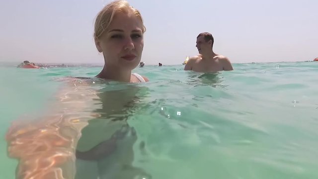 young beautiful blonde relieves herself on camera, standing in the water. Underwater and surface survey