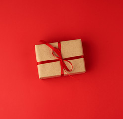 box wrapped in brown kraft paper and tied with a red thin silk ribbon on a red background
