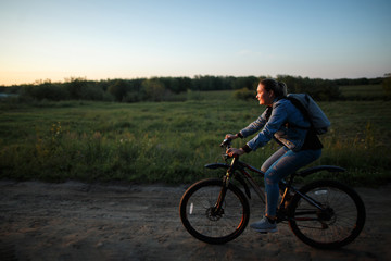 A woman rides her bike on a field road at sunset.