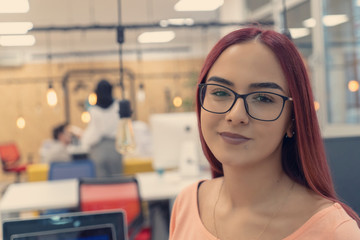 Portrait of young white woman in a busy modern workplace