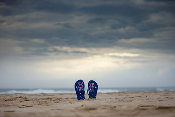 Australian thongs sticking upright in sand with dramatic storm clouds background. Australia day and...