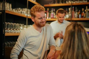 Handsome caucasian bearded ginger standing in bar with his female friend, chatting and having fun. Pub interior. Nightlife.