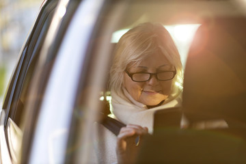 Senior woman with smartphone on the back seat of a car