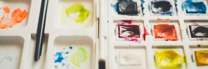 Used watercolor paint with brush in dirty white plastic container closeup.