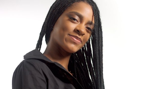 portrait of mixed race black woman with hair braids watching to the camera slightly smiling. contrast black look