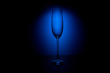 Empty champagne glass on a blue gradient background and with reflection on the surface