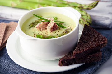 Asparagus soup with black bread in white bowl closeup. Food photography
