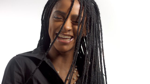 portrait of mixed race black woman with hair braids laughing with braids partly covered her face