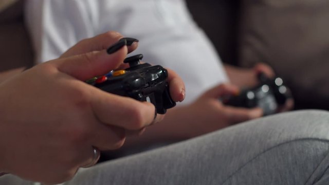 Close-up of mother and son playing video games at home together sitting on the couch, they are holding joysticks and compete. High resolution.