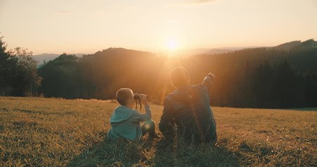 Happy traveler father and son sitting on grass and look through binoculars, bonding around mountain under sun light enjoying the leisure and freedom. 4K slow motion video