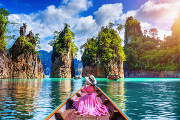 Beautiful girl sitting on the boat and looking to mountains in Ratchaprapha Dam at Khao Sok National Park, Surat Thani Province, Thailand. - obrazy, fototapety, plakaty