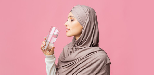 Arabic Girl Drinking Clean Mineral Water From Glass Over Pink Background