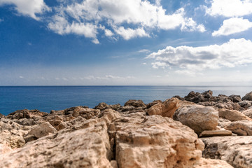 Mediterranean Sea in Northern Cyprus. Summer rocky coast, transparent calm blue water and white clouds on blue sky.