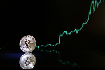 Bitcoin on the background of bullish stock chart on a black background. cryptocurrency coin on black background with reflection. increase in the value of bitcoin, dark photo.