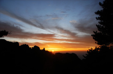 Huangshan Mountain in Anhui Province, China. Sunset over Huangshan with colorful sky and clouds, a silhouette of the mountain and foreground tree. Sunset near the summit of Huangshan Mountain, China.