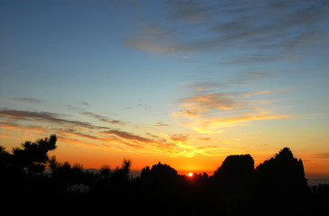 Huangshan Mountain in Anhui Province, China. Sunrise over Huangshan with a colorful sky, clouds, pine trees and silhouette of the mountain. Sunrise near the summit of Huangshan Mountain, China.