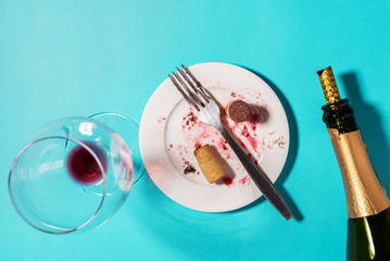 Conceptual background with objects left after a night party, an empty bottle of alcohol, a glass with the remnants of wine, dirty dishes on a blue background