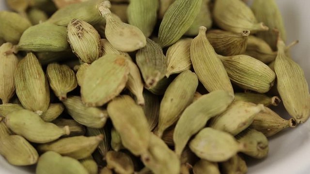 Cardamom fruits fall in a glass transparent bowl, close-up